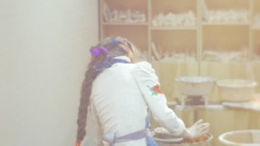 Kız Kalın Örgü Bir Kil Atölyesi nden Bir Hediye Yapma Hard Trying ile Bir Çömlekçilik Tekerlek Küçük Blonde Kız Dönen bir Clay Circle Kid's Back Çocuk Kalıplama olduğunu