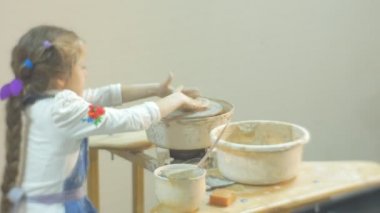 Kız bir çanak çömlek çarkı Concentratedly kil küçük sarışın kız kalıplama bacak tarafından dönen çalışırken zor bir hediye gelen bir kil içinde çanak çömlek Atölyesi yapıyor