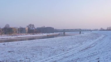 Bir nehir demiryolu köprüsü üzerinde bir yere pembe gökyüzü günbatımı bir nehir eski Metal konstrüksiyon kışlık manzara kar üzerinden tam tersi kıyısında evler