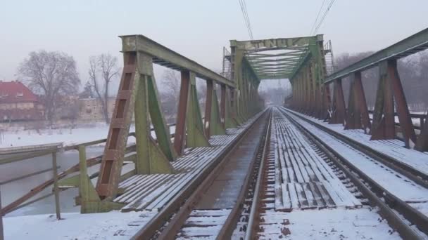 Inscription du pont vide dans l'ancien pont ferroviaire polonais à travers une rivière Constructions métalliques Maisons sur la rive opposée Paysage hivernal Neige au sol — Video