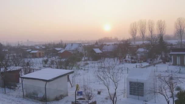 Panorama de uma Vila Pequenas Casas Ramos nus Árvores Pôr-do-sol Céu rosa Neve está em um terreno Wintry Lanscape Inverno Nublado Sol brilha através de nuvens cor-de-rosa — Vídeo de Stock