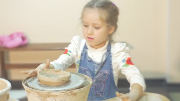 Kid tourne une roue de poterie à la main moulant un cercle d'argile sculptant un vase souriant Petite fille blonde faisant un cadeau dans un atelier de poterie — Video