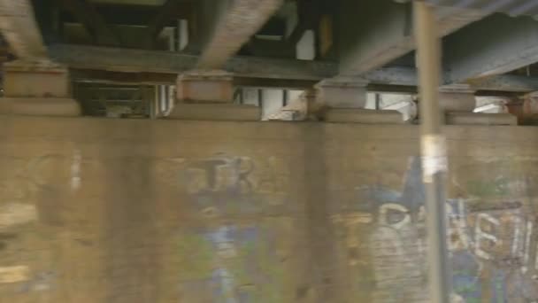 Las paredes están pintadas con graffiti Paseos en tren de carga por el puente a través de una carretera fluvial debajo del puente Señal de carretera Árboles sin hojas Nublado Invierno Kiev — Vídeos de Stock