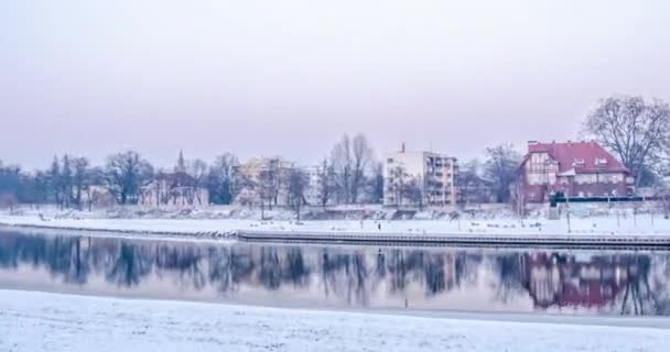 Casa con edificios de techo rojo Ramas desnudas Árboles en la orilla del río Hiperlapso Titelapse Modernos edificios de varios pisos en un horizonte Invierno Nieve Cielo gris — Vídeos de Stock