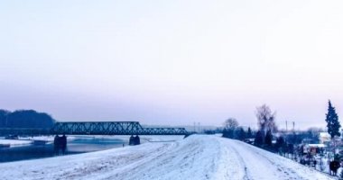 Kar demiryolu Köprüsü Hyperlapse Titelapse küçük evler ağaçlar çıplak dalları ağaçlar erken akşam kış gri gökyüzü arasında tarafından River yürüyüş adamdır