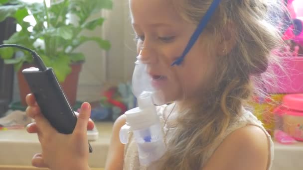 Girl Kid andas genom inhalator leker med mobiltelefon sitter med nebulisator mask på hennes ansikte håller en mobiltelefon ånga höjer upp — Stockvideo