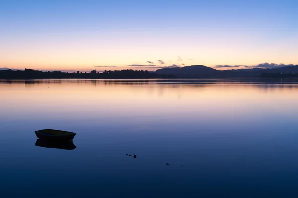 Pequeno barco flutuando na baía calma durante o nascer do sol brilhante . — Fotografia de Stock