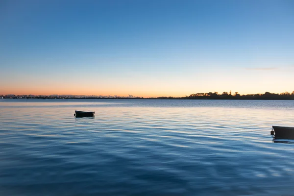 Sunrise across bay with small dinghy blue tones with orange arou — Stock Photo, Image