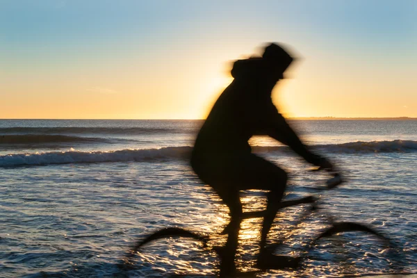 Blurred cyclist in motion riding along beach at sunrise. — Stock Photo, Image