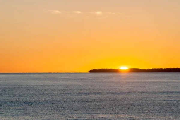 Cielo naranja brillante sobre el océano plano al amanecer con la isla baja brillando en el horizonte . — Foto de Stock