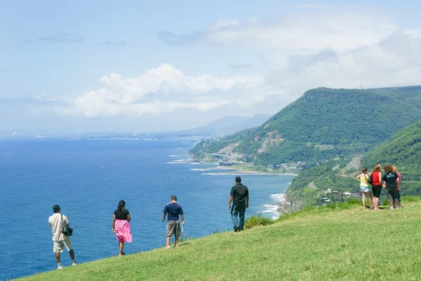 Los turistas se detienen a la vista y el distante puente del acantilado del mar a — Foto de Stock