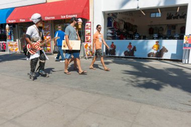 Los Angeles USA _ 6 Ekim 2015; İnsanlar gitar çalarak paten kayarken turistler yolda yürüyor.