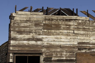 Eski binanın ahşap perdesi çöl mavisi gökyüzünün altında çürümeye terk edilmiş..