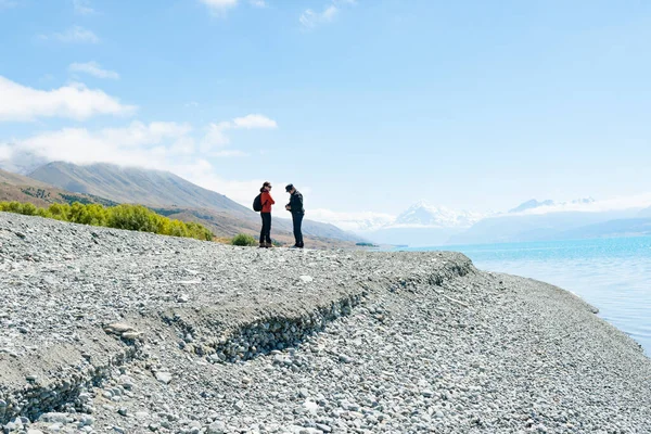 Lake Pukaki New Zealand February 15 2015; two female tourists standing on grey stony lake edge and turquoise blue water of snow feed scenic Lake Pukaki in South Ilsand New Zealand.