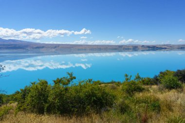 Pukaki Gölü 'nün turkuaz mavi suyu, uzun beyaz bulut yansımaları.