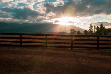 Karanlık çiftlikteki çit ve çit batan güneşle aydınlatılıyor.