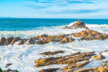 Yeni Zelanda 'daki Maunganui Dağı' nın engebeli tabanında dalgalı deniz dalgaları Kuzey Kayası 'nın etrafını sarar..