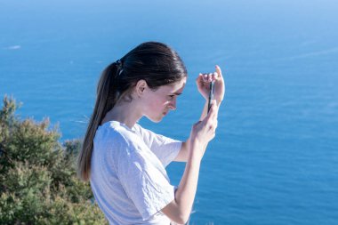 Maunganui Dağı 'nın tepesindeki genç, ekranı mavi okyanusla gölgelendirirken aygıtı kontrol ediyor.
