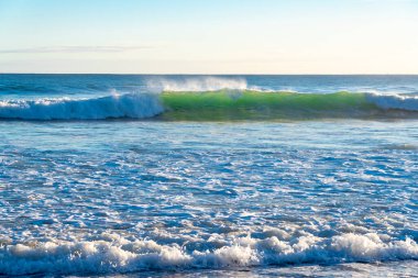 Kıyı sahnesinde dalgalar ve kumsal köpüğü kırılıyor..