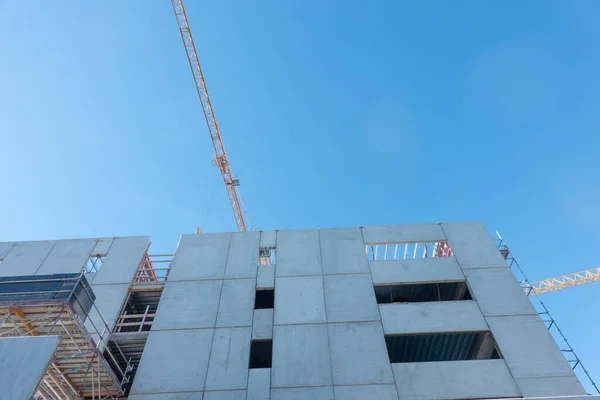 Closeup of construction of building with tall concrete panel wall with window openings and yellow crane in Tauranga, New Zealand.