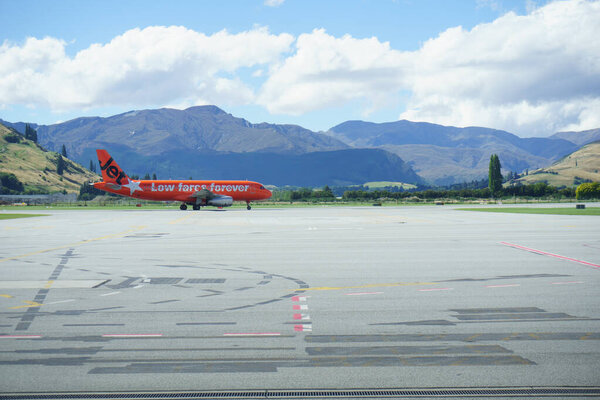 Queenstown, New Zealand - March 6 2015; Mountains form backdrop to orange color plane arriving at airport .