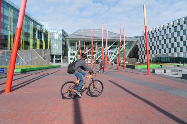 DUBLIN, IRELAND - 10 AĞUSTOS 2017; İşe giderken çevresi modern mimari binalar ve kırmızı direk heykeliyle çevrili Grand Canal Meydanı 'nda yürüyen banliyö bisikletleri