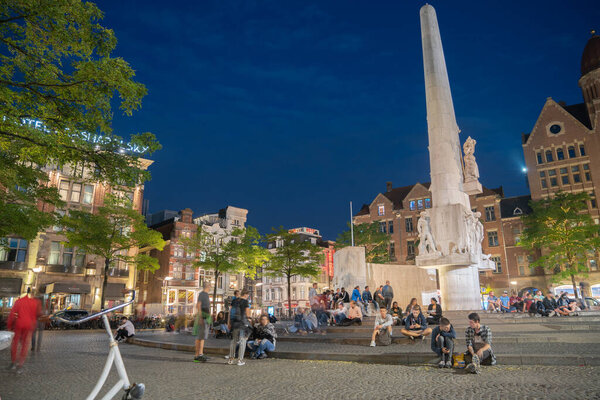 Amsterdam Netherlands - August 17 2017 Tall white structure in Dam Square,  Dutch National Monument illuminated at night with tourists in street.