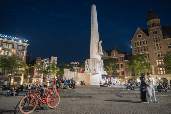 Amsterdam Netherlands - August 17 2017; Long exposure tall white structure in Dam Square, Dutch National Monument illuminated at night with tourists in street.
