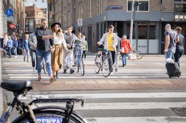Amsterdam-Hollanda - 21 Ağustos 2017; Aralarında siyah şapkalı kadın ve kasıtlı olarak yürüyen erkek de dahil olmak üzere insanlar caddeyi geçerken, diğerleri torba sürüklüyor..