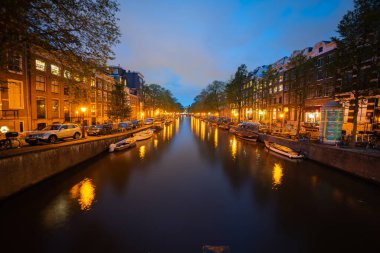 Amsterdam-Hollanda - 21 Ağustos 2017; Peri dünyası gece ışıkları gibi şehir kanallarını ve çevreleyen binaları aydınlatıyor