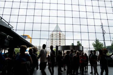 Rotterdam Hollanda - Ağustos 2017; İnsanlar şehrin modern apartmanlarından birinin Rotterdam Çarşı Salonu 'ndan görülebildiği büyük pencerenin dış ışığına karşı siluet karıştırıyor, yuvarlak çatı profilli modern yapı