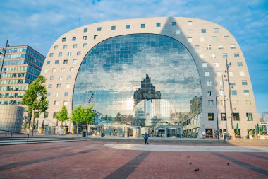 Rotterdam Hollanda - 23 Ağustos 2017; Güneş batarken ve kaldırımda uzun gölgeler bırakırken, dört katlı Pazar Salonu cam cephe önü gökyüzünü ve etrafındaki binaları yansıtıyor