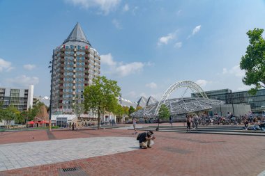Rotterdam Hollanda - 22 Ağustos 2021; Rotterdam Çarşı Salonu 'nun yanında şehir manzarası açık, arka planda uzun apartman binası ve cep telefonuyla fotoğraf çeken turist çömelmiş..