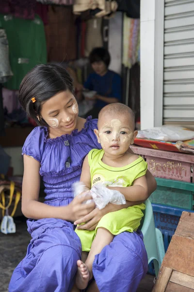 Молодая азиатка с танакой на лице, держащая ребенка на коленях — стоковое фото