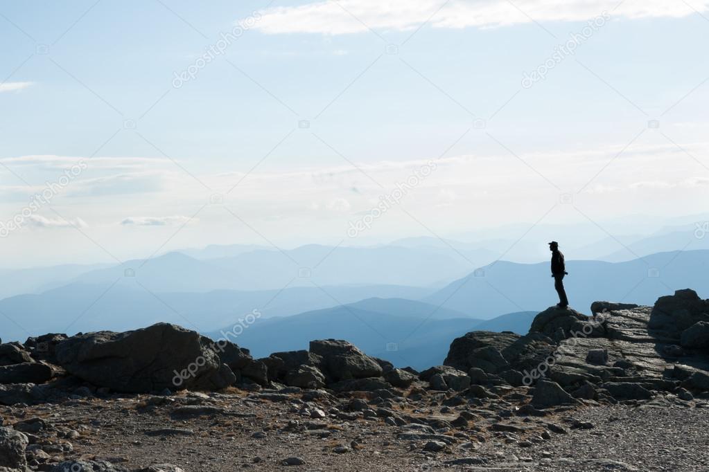 On mountain top, silhouette of man, unrecognisable stands on rock looking into the view.