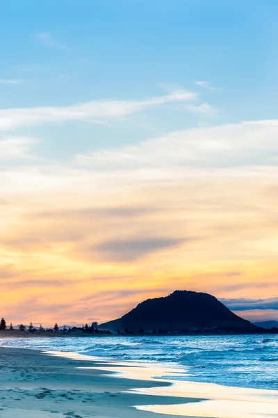 Ställa in solen kastar blå nyans på vattnet och stranden och orange moln — Stockfoto