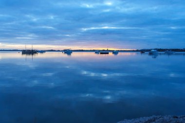 Sakin ve bulutlu Tauranga limanı boyunca uzanan manzara bulutlu gökyüzünün altında altın saate dönüşüyor..