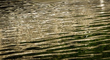 Soyut arkaplan, güneş doğarken mavi ve altın su yüzeyindeki ışık desenlerini yansıtıyor..