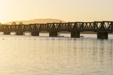 Tauranga Yeni Zelanda - 2 Aralık 2025; Altında hafif kürekçiler siluet tarihi kiriş demiryolu köprüsünün altından geçmekte.
