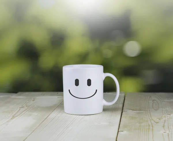 Tazza di caffè bianco sorridente su tavolo in legno con backgroun verde bokeh — Foto Stock