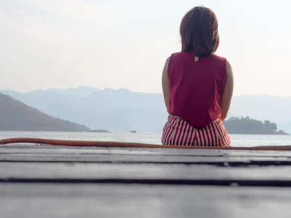 Дівчина сидить на дерев'яному балконі, з морем і горою, подорожувати назад — стокове фото