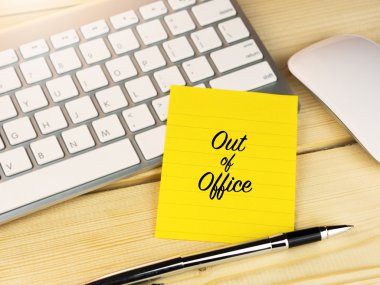 Out of office on sticky note on work desk clipart