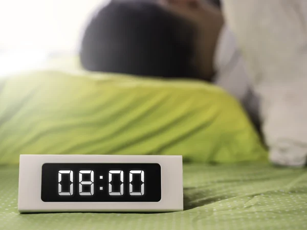 8 часов на цифровых часах с мужчиной, спящим на заднем плане — стоковое фото