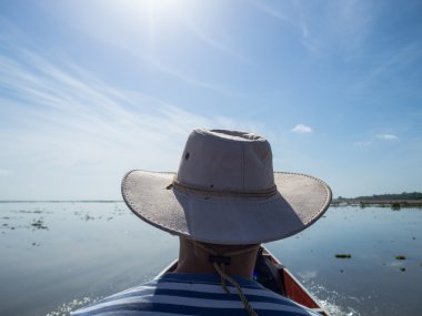 Nehir teknesinde oturan şapkalı adam arka