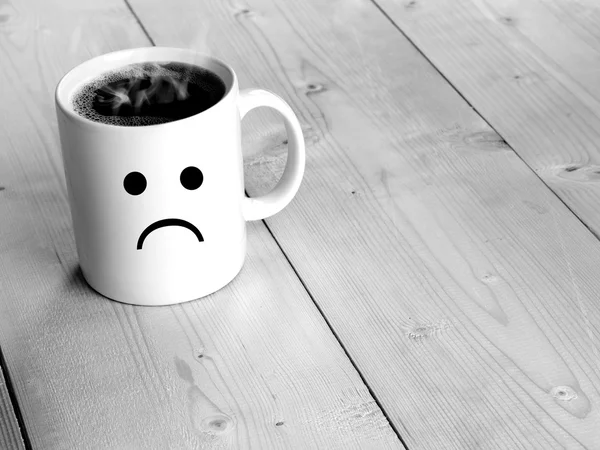 Preto e branco de cara triste na caneca ou xícara de café na mesa de madeira — Fotografia de Stock