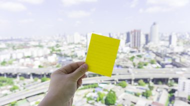 Kentsel sahne ve gökyüzü ile tutan el üzerinde yeşil yapışkan not