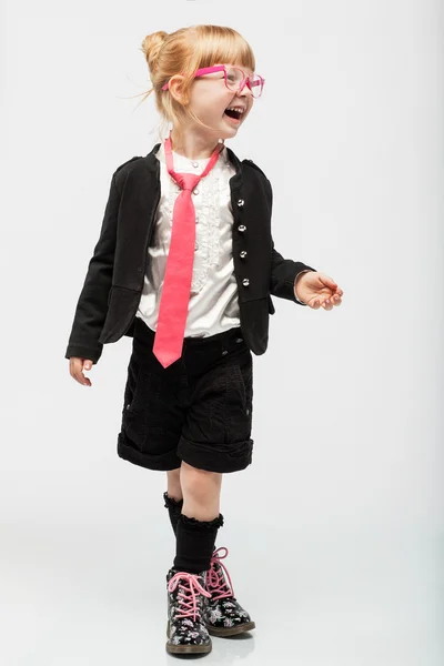 Güzel genç küçük kız ayakta siyah şort, ceket, beyaz gömlek, pembe gözlük ve kravat gülümseyen.