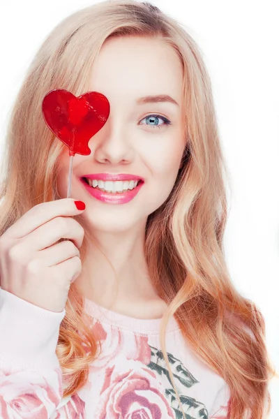 Kırmızı bir lolipop kalp şeklinde alarak studio beyaz arka planda poz mutlu sarışın kız.