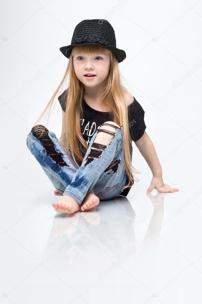 Beautiful little happy redhead girl sitting on the floor posing in studio white background in black shirt.