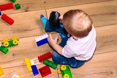 Yerde oturan küçük çocuk tasarımcıyla oynuyor..